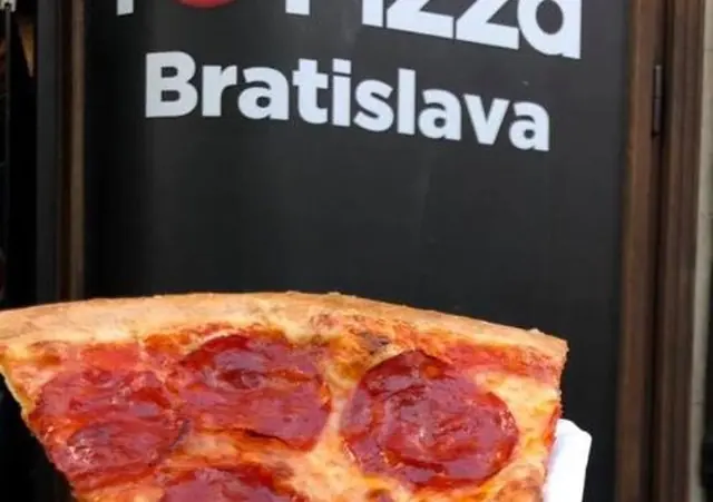 Ruka drží kúsok pizze so salámou na papierovom obrúsku pred čiernym nápisom I Love Pizza Bratislava