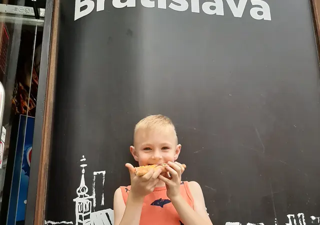 Chlapec je kúsok pizze pred čiernou stenou s nápisom I Love Pizza Bratislava