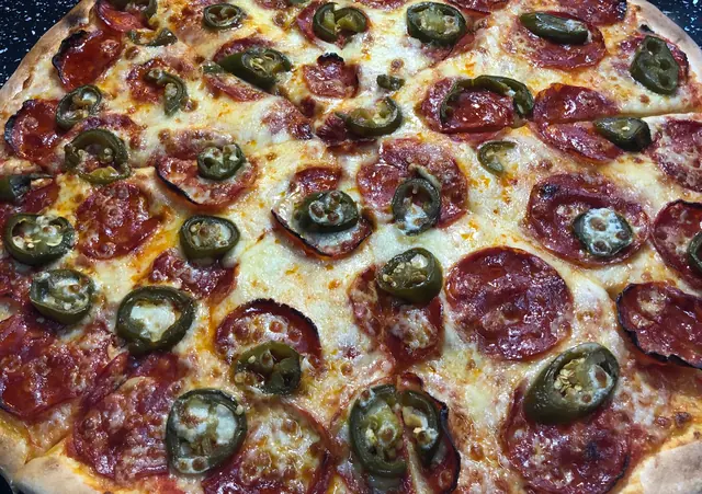 Celá pizza so salámou a jalapeňos na pulte, v pozadí ďalšie pizze