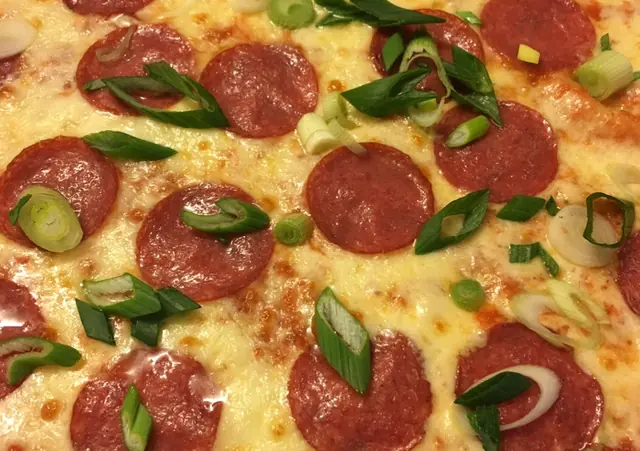 Detail pizze so salámou, roztopenou mozzarellou a jarnou cibuľkou