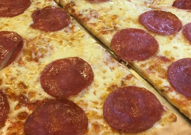 Pizza so salámou nakrájaná na veľké kúsky v štýle New York na pulte s ďalšími pizzami