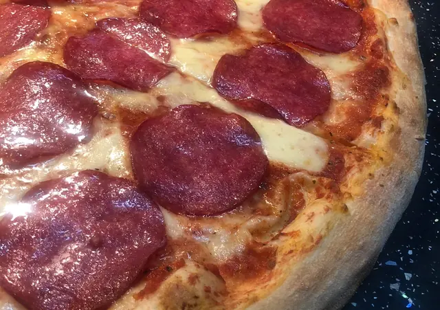 Detail pizze so salámou a roztopenou mozzarellou na tmavom pulte