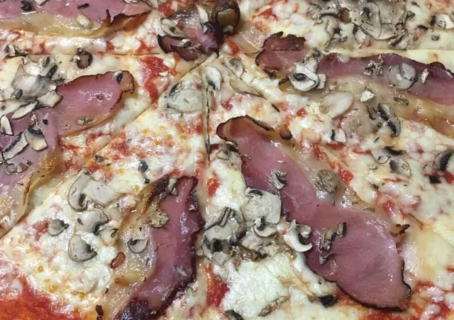 Pizza nakrájaná na kúsky, so šunkou, šampiňónmi a roztopenou mozzarellou