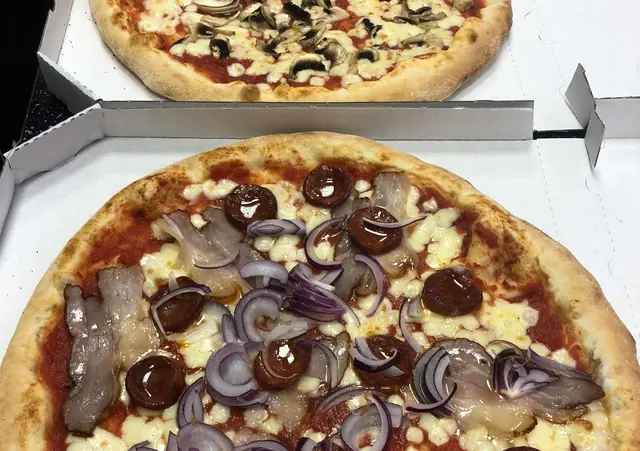 Dve pizze v kartónových krabiciach: jedna so šampiňónmi, druhá so slaninou, chorizom a červenou cibuľou