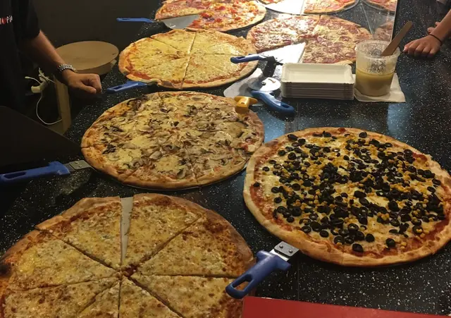 Dlhý pult v prevádzke plný celých pizz s olivami, šampiňónmi a syrom
