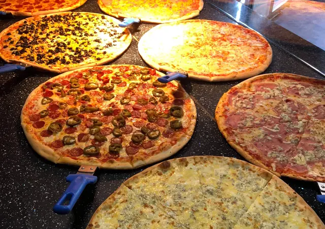 Pult s viacerými druhmi čerstvo upečenej pizzy pod ohrievacími lampami