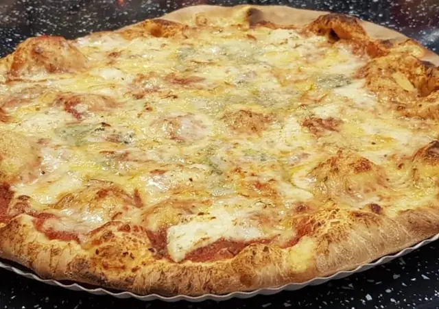 Syrová pizza s nivou a zlatistým okrajom na tácke na tmavom pulte
