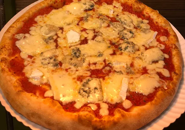 Syrová pizza s nivou a ďalšími syrmi na papierovom tanieri pred drevenou stenou