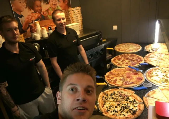 Tím I Love Pizza v čiernych polokošeliach s logom pri pulte s čerstvo upečenými pizzami